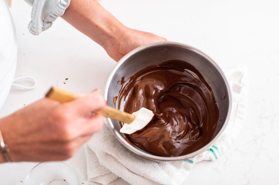 Baker stirring bowl of melted chocolate with a spatula